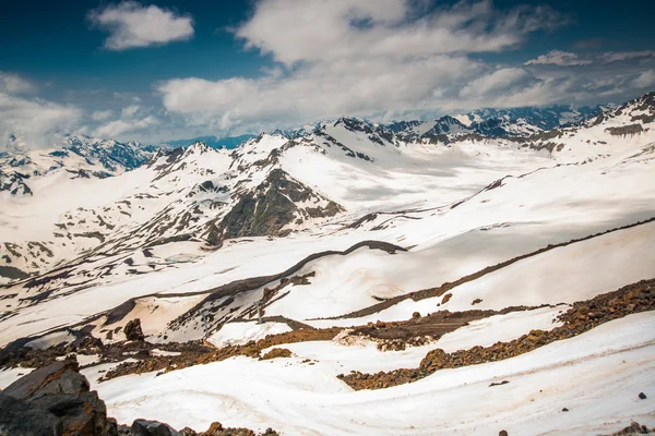 Sneeuw op de bergen tegen de blauwe hemel in de wolken. De Elbroes regio. De Kaukasus. — Stockfoto