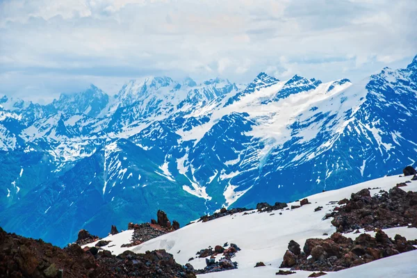 Sneeuw op de bergen tegen de blauwe hemel in de wolken. De Elbroes regio. De Kaukasus. — Stockfoto