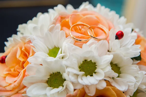 Trauringe liegen auf einem Strauß orangefarbener Rosen und weißer Farben. Marienkäfer. — Stockfoto