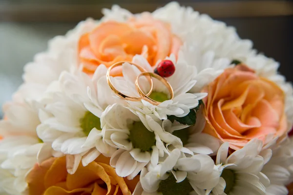 Trouwringen liggen op een boeket van Oranje Rozen en witte kleuren. Lieveheersbeestje. — Stockfoto