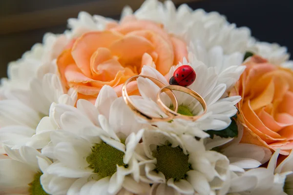 Obrączki ślubne leżą na bukiet róż pomarańczowy i biały kolory. Biedronka. — Zdjęcie stockowe