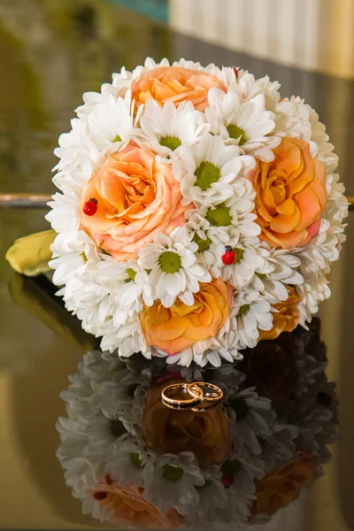 Anillos de boda se encuentran en un ramo de rosas naranjas y colores blancos . — Foto de Stock