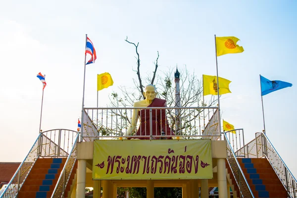 Sculptuur van een monnik en de multi-gekleurde vlaggen bij de tempel. Thailand. — Stockfoto