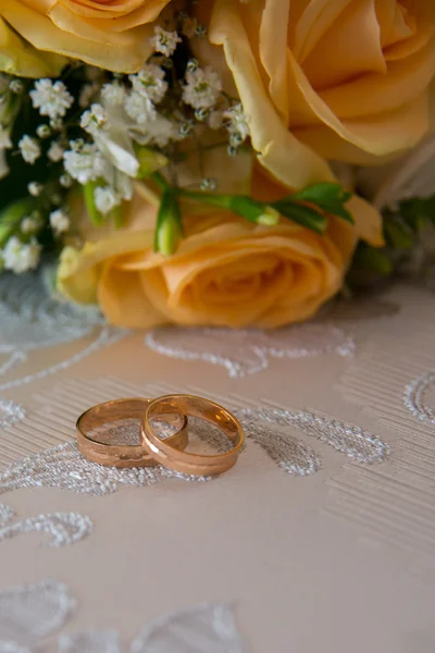 Due fedi nuziali d'oro si trovano sul tavolo vicino al bouquet di rose arancioni e fiori bianchi . — Foto Stock