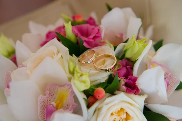 Dos anillos de oro de la boda con un diamante que miente en el ramo de la novia de orquídeas blancas y flores rosadas . — Foto de Stock