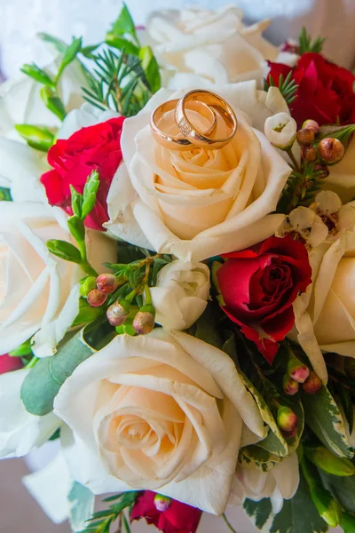 Dos anillos de oro de boda con diamantes están en el ramo de rosas rojas y blancas de la novia . — Foto de Stock