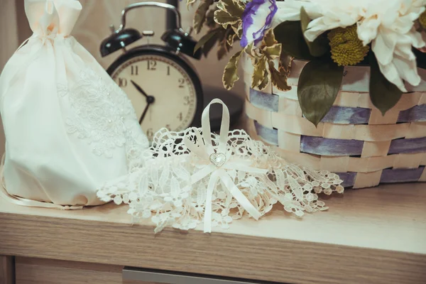 Lace bruiloft Kousenband en witte handtas van de bruid zijn ons de tabel bij de wekker. — Stockfoto