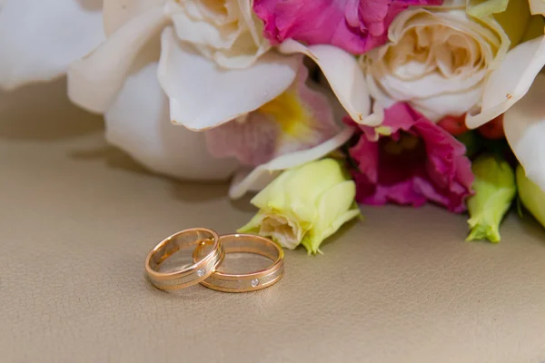 Dois anéis de casamento de ouro com diamante jazem em torno do buquê da noiva de orquídeas brancas e flores rosa . — Fotografia de Stock