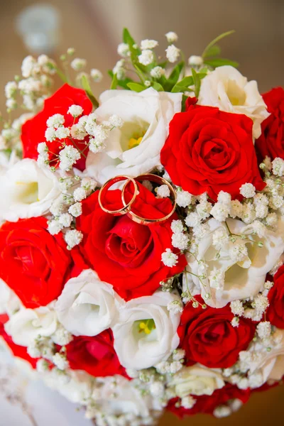 Dos anillos de boda de oro se encuentran en un ramo de rosas rojas y blancas . — Foto de Stock