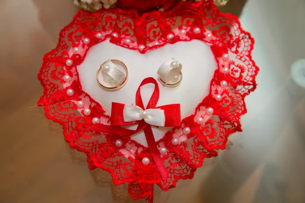 两个金色的结婚戒指躺在一个用红色蕾丝表示心脏形状的垫子上 — 图库照片