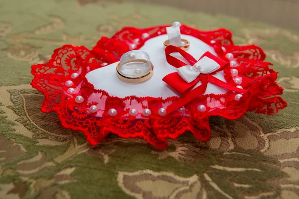 Dos anillos de boda de oro se encuentran en un cojín en forma de corazón con un encaje rojo — Foto de Stock