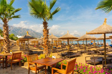 Kemer 'in merkez plajında plaj şemsiyeleri ve palmiye ağaçları, arka planda dağlar, Antalya, Türkiye.
