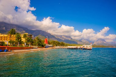 KEMER, TURKEY: Türkiye 'nin Akdeniz kıyısındaki popüler turizm beldesi Kemer' de güneşli bir günde plaj ve dağ manzaralı manzara.
