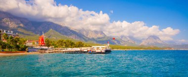 KEMER, TURKEY: Türkiye 'nin Akdeniz kıyısındaki popüler turizm beldesi Kemer' de güneşli bir günde plaj ve dağ manzaralı manzara.