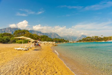 KEMER, TURKEY: Türkiye 'nin Akdeniz kıyısındaki popüler turizm beldesi Kemer' de güneşli bir günde plaj ve mavi deniz manzaralı cennet manzarası.
