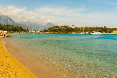 KEMER, TURKEY: Türkiye 'nin Akdeniz kıyısındaki popüler turizm beldesi Kemer' de güneşli bir günde plaj ve mavi deniz manzaralı cennet manzarası.