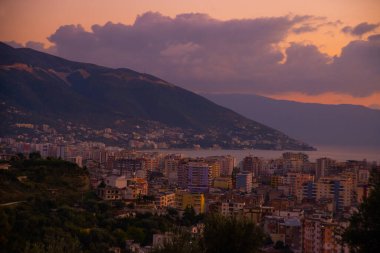 VLORA, ALBANIA: Cityscape seen from Kuzum Baba hill. Aerial city view, city panorama of Vlore at sunset, Albania. clipart