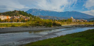 BERAT, ALBANIA: Berat Üniversitesi manzarası, çiçek açan ağaçlar ve Osum Nehri kıyısından Tomorr Ulusal Parkı dağları.