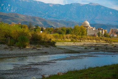 BERAT, ALBANIA: Berat Üniversitesi manzarası, çiçek açan ağaçlar ve Osum Nehri kıyısından Tomorr Ulusal Parkı dağları.