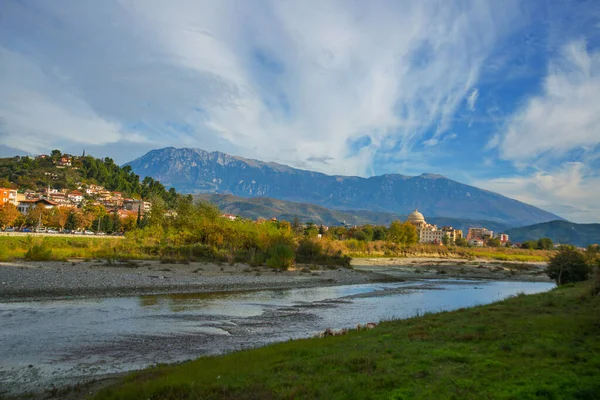 BERAT, ALBANIA: Berat Üniversitesi manzarası, çiçek açan ağaçlar ve Osum Nehri kıyısından Tomorr Ulusal Parkı dağları.