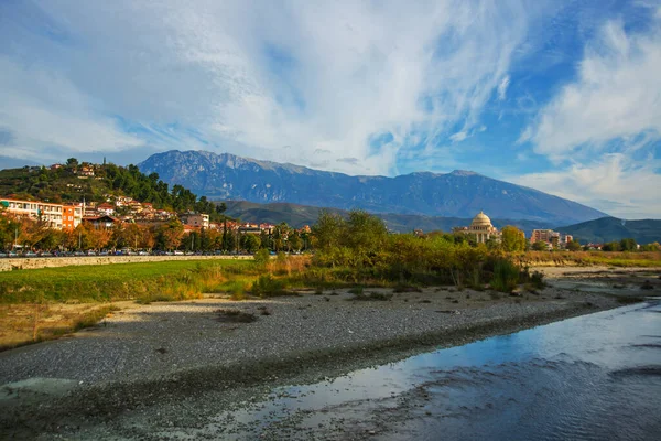 BERAT, ALBANIA: Berat Üniversitesi manzarası, çiçek açan ağaçlar ve Osum Nehri kıyısından Tomorr Ulusal Parkı dağları.