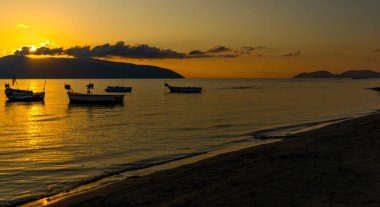 VLORA / VLORE, ALBANIA: Denizde güzel gün batımı, güneşin arka planında balıkçı tekneleri siluetleri.