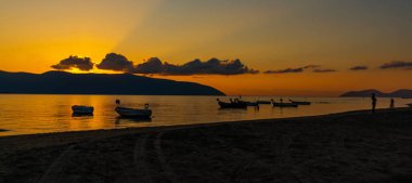 VLORA / VLORE, ALBANIA: Denizde güzel gün batımı, güneşin arka planında balıkçı tekneleri siluetleri.