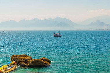 Türkiye 'nin Antalya kentinde güneşli bir yaz gününde Akdeniz kıyısında turistlerle dolu güzel bir gemi yelken açıyor.