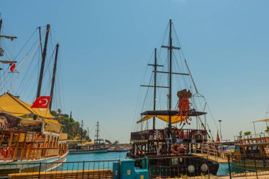 Mavi gökyüzü ve denizin arka planında, korsan olarak süslenmiş bir eğlence gemisi yelkenlisi. Gemi, Antalya limanından turistleri kıyı şeridi etrafında bir geziye çıkarıyor..