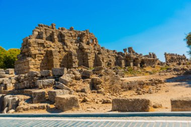 Eski harabeler ve güneşli bir yaz gününde, Kenar mahallesinde mavi bir gökyüzünün arka planına karşı bir yol. Yana, Antalya ili, Türkiye.