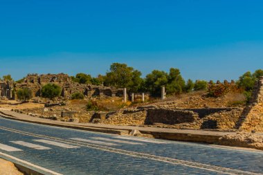 Eski harabeler ve güneşli bir yaz gününde, Kenar mahallesinde mavi bir gökyüzünün arka planına karşı bir yol. Yana, Antalya ili, Türkiye.