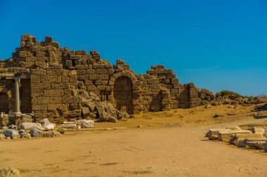 Eski harabeler ve güneşli bir yaz gününde, Kenar mahallesinde mavi bir gökyüzünün arka planına karşı bir yol. Yana, Antalya ili, Türkiye.