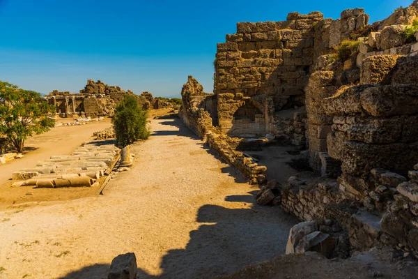 Eski harabeler ve güneşli bir yaz gününde, Kenar mahallesinde mavi bir gökyüzünün arka planına karşı bir yol. Yana, Antalya ili, Türkiye.