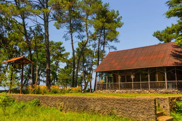 KOBULETI, GEORGIA: Houten orthodoxe kerk in een schaduwrijk park op een zonnige zomerdag. — Stockfoto