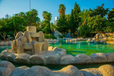 Güneşli bir yaz gününde Türkiye 'nin Antalya kentinin merkezinde fıskiyeli ve göletli güzel bir parkın manzarasıyla manzara.