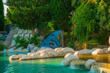 Güneşli bir yaz gününde Türkiye 'nin Antalya kentinin merkezinde fıskiyeli ve göletli güzel bir parkın manzarasıyla manzara.