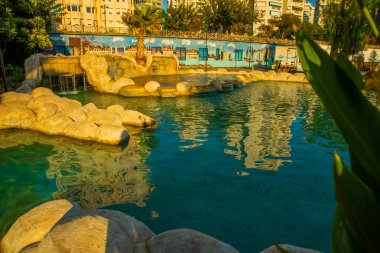 Güneşli bir yaz gününde Türkiye 'nin Antalya kentinin merkezinde fıskiyeli ve göletli güzel bir parkın manzarasıyla manzara.