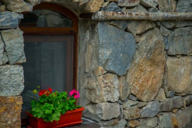 Taş Manastırı. Taş duvar arka plan üzerinde bir pencere. Kırmızı çiçekler bir tencerede. Caucasus.Russia.