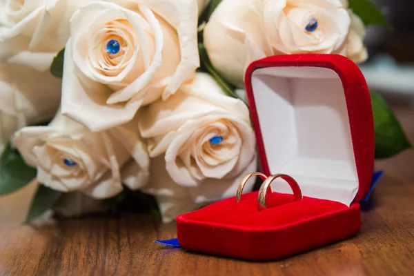 Two wedding rings in red box lying on the bouquet of white roses — Stock Photo, Image