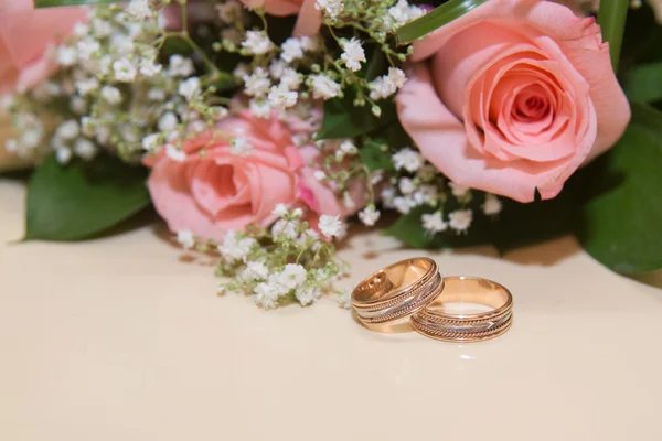 Duas alianças de casamento estão na mesa.Beckett rosa rosas . — Fotografia de Stock