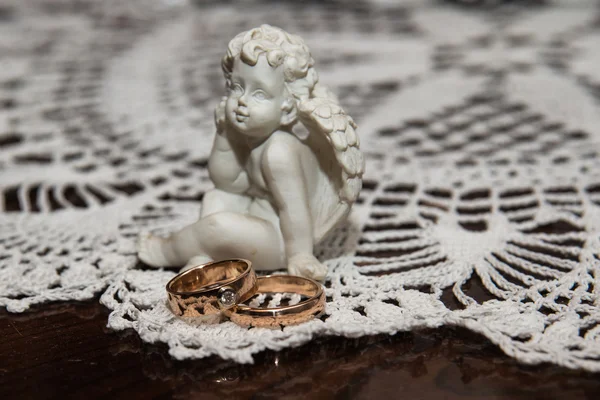 Dois anéis de casamento jazem sobre a mesa.Um anjo de escultura . — Fotografia de Stock