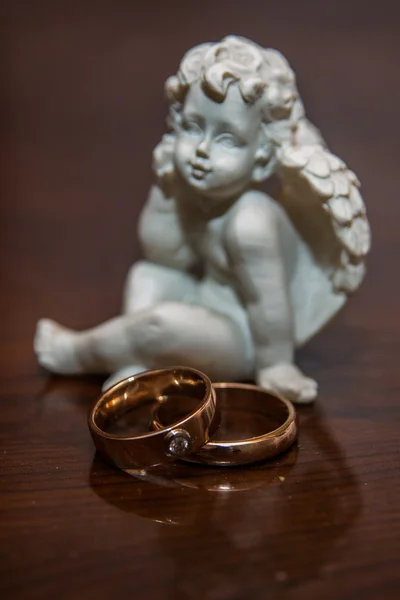 Dva snubní prsteny ležet na stole. Socha anděla. — Stock fotografie