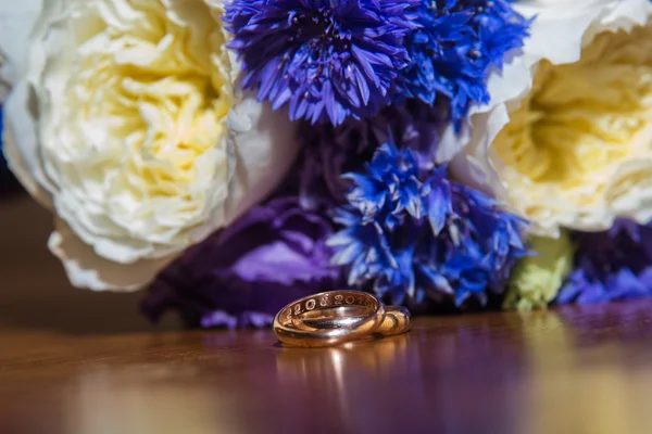 Due fedi nuziali e un bouquet di fiori blu, bianchi e viola . — Foto Stock