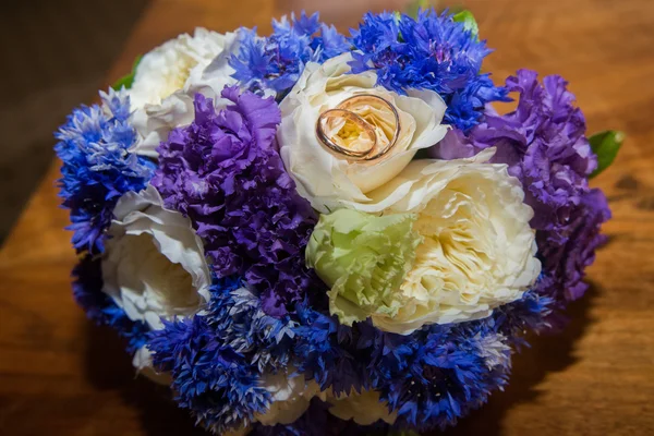 Twee trouwringen en een boeket van blauw, wit en paarse bloemen. — Stockfoto