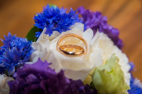 Dois anéis de casamento e um buquê de flores azuis, brancas e roxas . — Fotografia de Stock