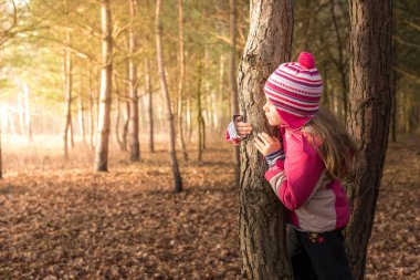 Kız ağacın arkasına saklanıyor.