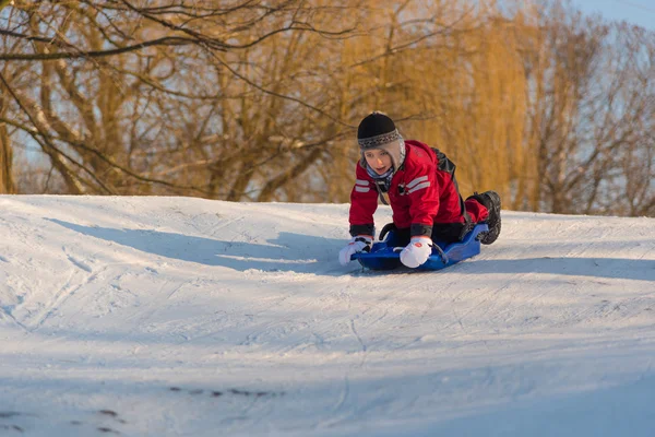 Little boy kneeling on sledge and riding down a slope — Stock Photo, Image