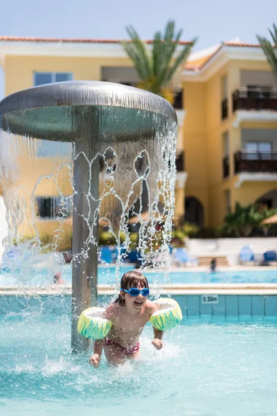 Happy little girl playing under swimming pool fountain