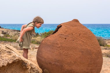 A girl looking into a giant old pot on Nissi Beach, Ayia Napa, C clipart