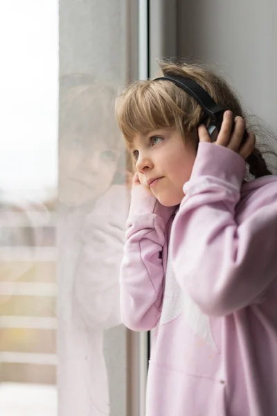 Girl with headphones looking through window — Stock Photo, Image